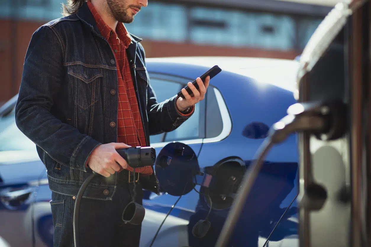 Man plugging in an EV charger and holding mobile phone to pay image