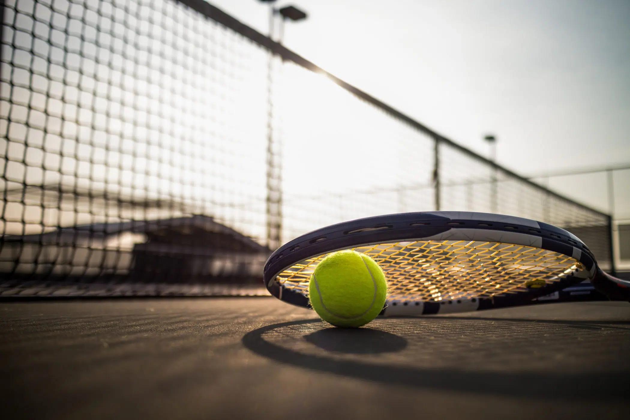 Tennis ball and racket on hard court under sunlight image