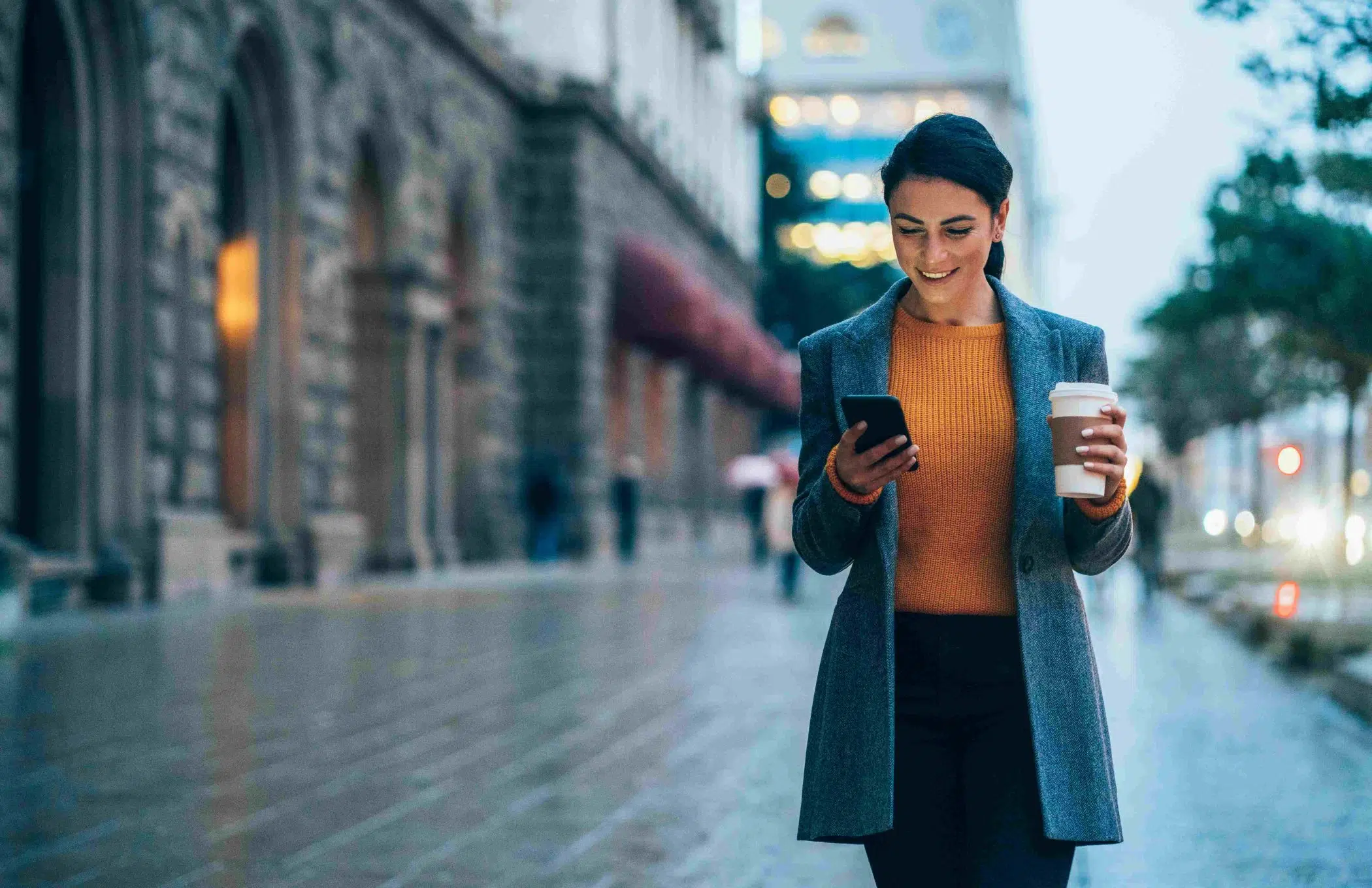 woman holding coffee whilst looking at phone on street image