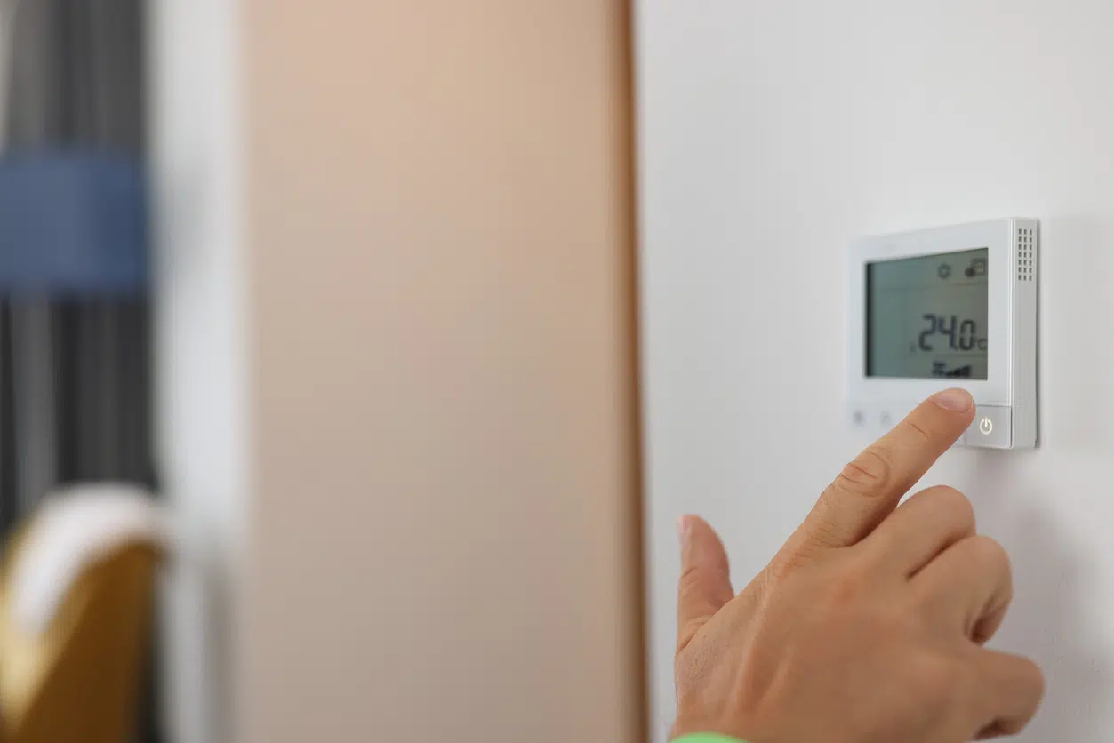 Hand sets a programmable thermostat for heating and cooling image