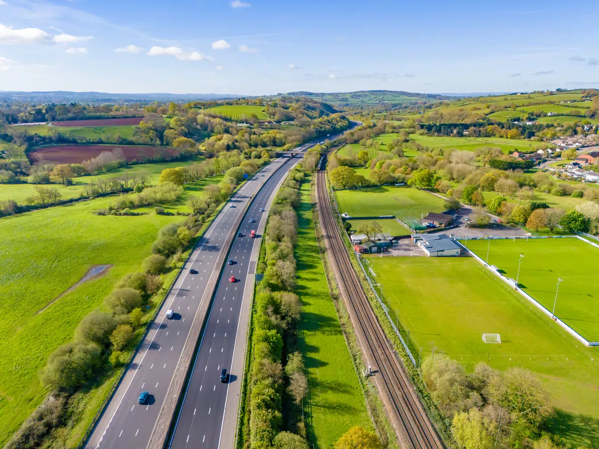Motorway and trainline running side by side across green fields