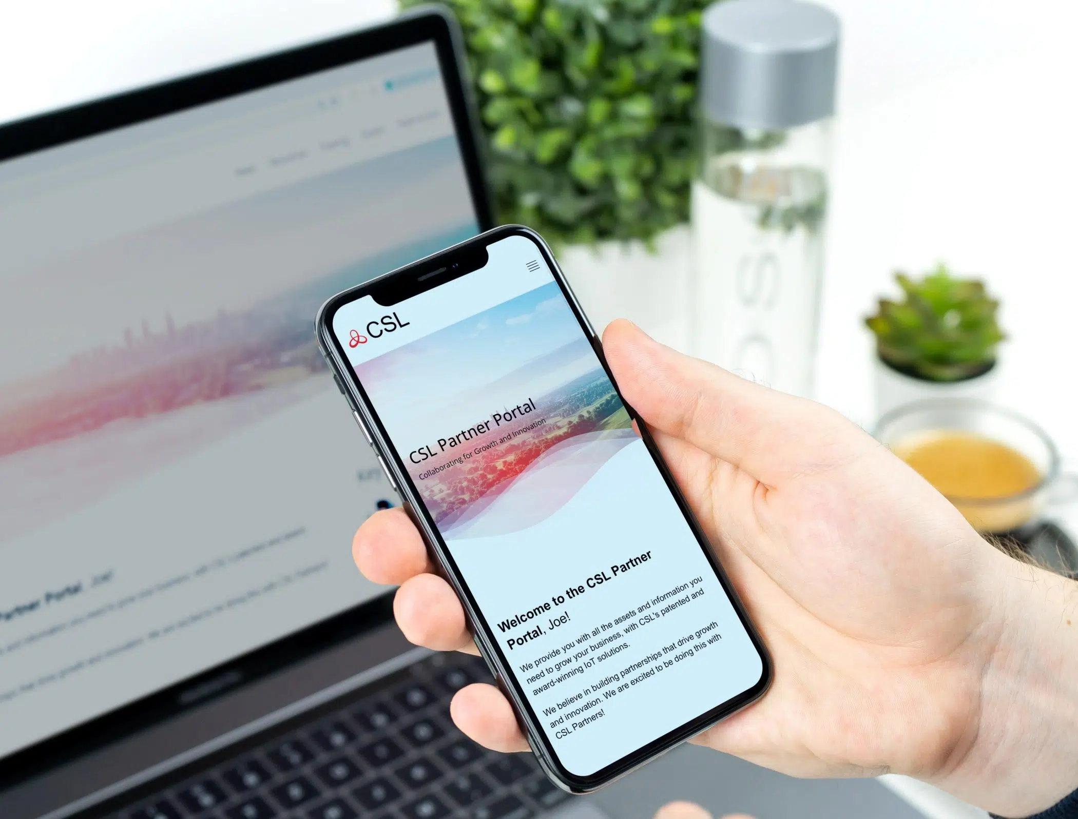 CSL-Partnerportal auf einem Mobiltelefon, das über einem Laptop gehalten wird.