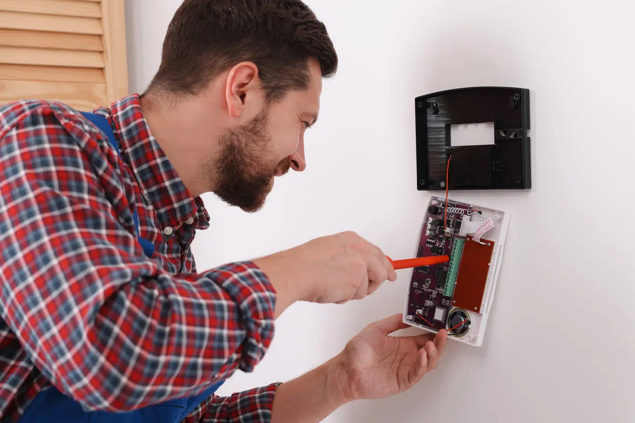 Technician installing home security alarm system on white wall indoors